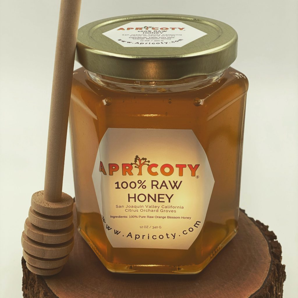 A jar of honey with a honey dip stick on a stump