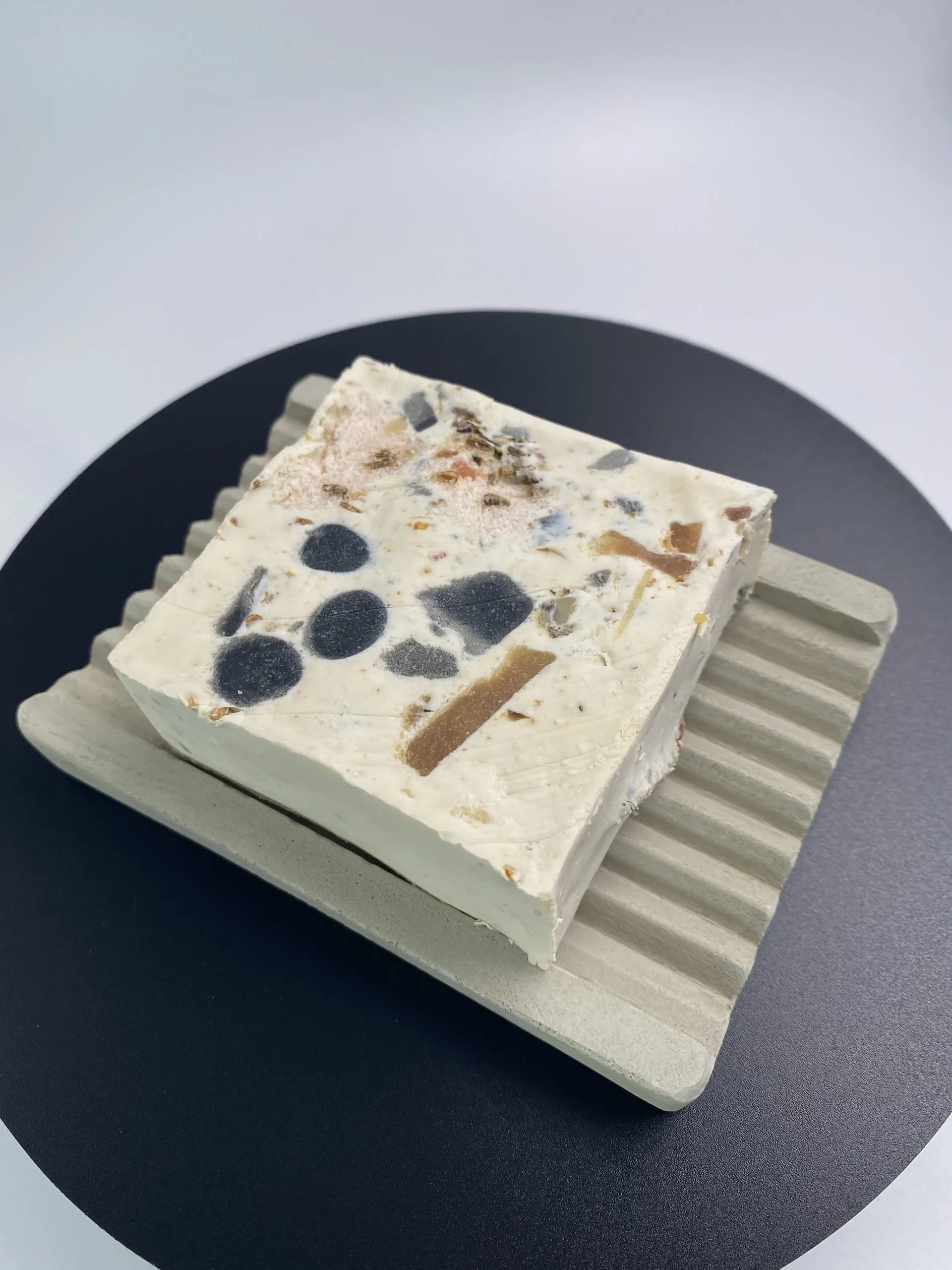 Apricoty handmade botanical soap bar resting on a grooved grey concrete soap dish