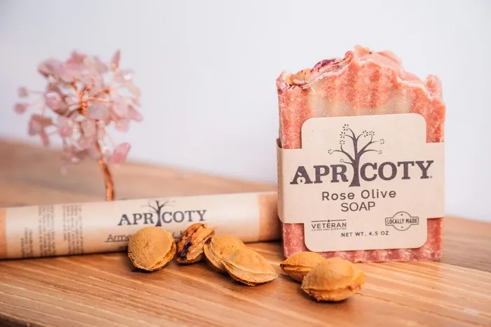 Apricoty Rose Olive Soap bar on a wooden table with apricot pits and a decorative crystal tree.